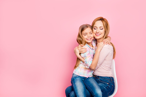 Close up portrait of lovely, charming daughter sitting on mom's hands over pink background, embracing with mum, close eyes, leisure, holidays, weekend, comfort, mother, women's day
