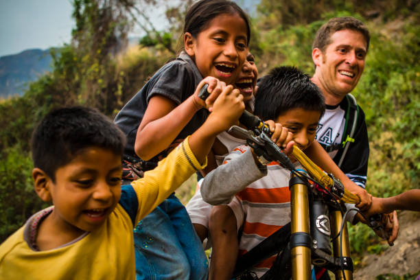 turysta pcha lokalne dzieci na rowerze. - guatemalan culture zdjęcia i obrazy z banku zdjęć