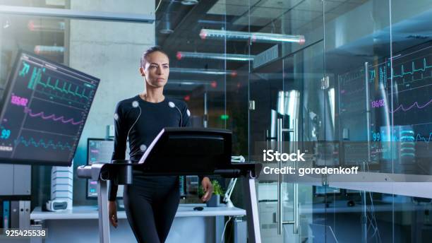 Beautiful Woman Athlete With Electrodes Connected To Her Body Walks On A Treadmill In A Sports Science Laboratory In The Background Hightech Laboratory With Monitors Showing Ekg Readings Stock Photo - Download Image Now