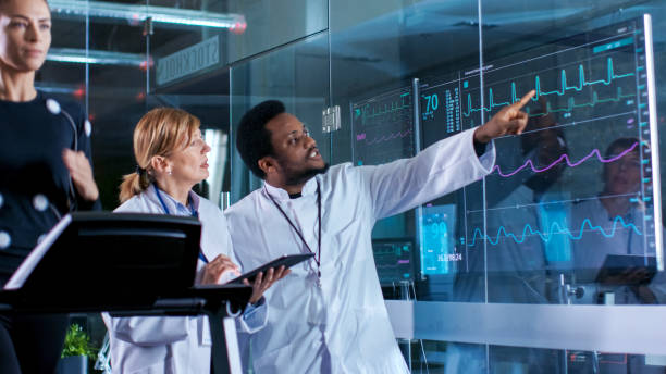 Beautiful Woman Athlete Runs on a Treadmill with Electrodes Attached to Her Body, while Two Scientists Supervise Watching EKG Data Showing on Laboratory Monitors. Beautiful Woman Athlete Runs on a Treadmill with Electrodes Attached to Her Body, while Two Scientists Supervise Watching EKG Data Showing on Laboratory Monitors. biomechanics stock pictures, royalty-free photos & images