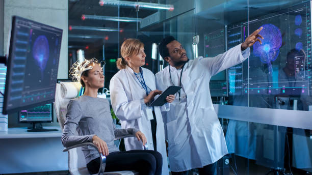 istock Woman Wearing Brainwave Scanning Headset Sits in a Chair while Two Scientists Supervise and Look at Data. In the Modern Brain Study Laboratory Monitors Show EEG Reading and Brain Model. 925425692