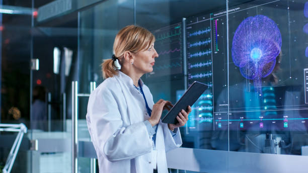 Female Scientist Uses Tablet Computer In the Modern Brain Study Laboratory and Monitors EEG Reading and Brain Model Functioning.