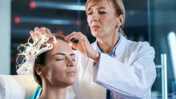 Close-up shot of a Woman Wearing Brainwave Scanning Headset Sits in a Chair while Scientist Adjusts the Device. In the Modern Brain Study Laboratory Monitors Show EEG Reading and Brain Model. Close-up shot of a Woman Wearing Brainwave Scanning Headset Sits in a Chair while Scientist Adjusts the Device. In the Modern Brain Study Laboratory Monitors Show EEG Reading and Brain Model. headphones plugged in photos stock pictures, royalty-free photos & images