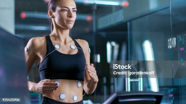 Beautiful Woman Athlete Runs On A Treadmill With Electrodes Attached To Her Body Female Physician Uses Tablet Computer And Controls Ekg Data Showing On Laboratory Monitors Stock Photo - Download Image Now