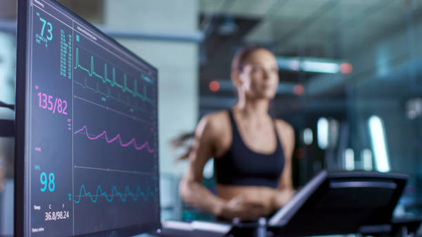 monitor médico muestra lectura de electrocardiograma de una mujer atleta corriendo en una cinta rodante. se centran en el monitor. - biomecánica fotografías e imágenes de stock