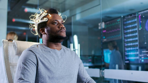 Man Wearing Brainwave Scanning Headset Sits in a Chair in the Modern Brain Study Laboratory Monitors Show EEG Reading and Brain Model. Man Wearing Brainwave Scanning Headset Sits in a Chair in the Modern Brain Study Laboratory Monitors Show EEG Reading and Brain Model. headphones plugged in photos stock pictures, royalty-free photos & images