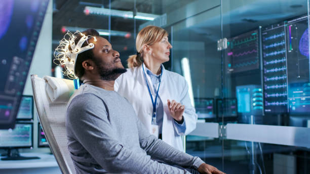 istock Man Wearing Brainwave Scanning Headset Sits in a Chair while Scientist Adjusts the Device. In the Modern Brain Study Laboratory Monitors Show EEG Reading and Brain Model. 925426164