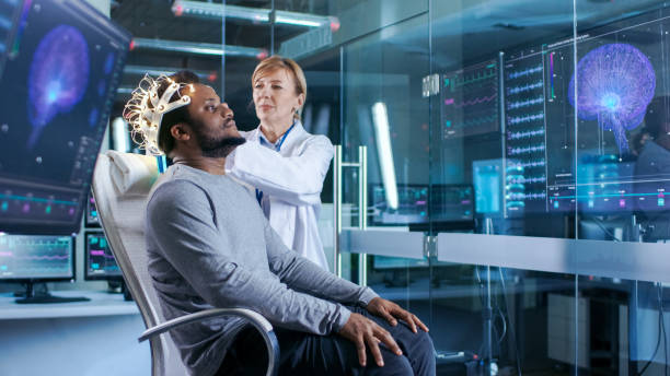 istock Man Wearing Brainwave Scanning Headset Sits in a Chair while Scientist Adjusts the Device. In the Modern Brain Study Laboratory Monitors Show EEG Reading and Brain Model. 925426180