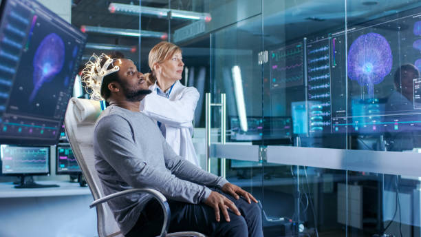 istock Man Wearing Brainwave Scanning Headset Sits in a Chair while Scientist Adjusts the Device. In the Modern Brain Study Laboratory Monitors Show EEG Reading and Brain Model. 925426198