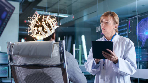 istock Man Wearing Brainwave Scanning Headset Sits in a Chair while Scientist with Tablet Computer Supervises Process. In the Modern Brain Study Laboratory Monitors Show EEG Reading and Brain Model. 925426226