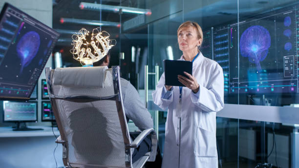 istock Man Wearing Brainwave Scanning Headset Sits in a Chair while Scientist with Tablet Computer Supervises Process. In the Modern Brain Study Laboratory Monitors Show EEG Reading and Brain Model. 925426232