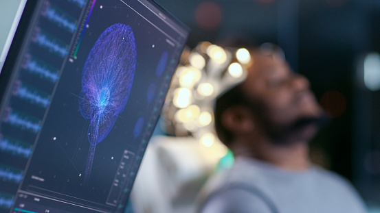 Monitores muestran modelo cerebro gráfica y lectura de EEG. En el hombre de laboratorio fondo usar ondas cerebrales exploración auricular se sienta en una silla con los ojos cerrados. En el laboratorio de investigación de estudio de cerebro moderno photo
