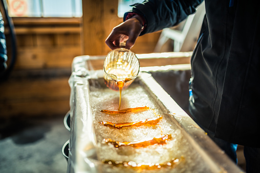 Person pouring maple syrup onto snow at sugar shack