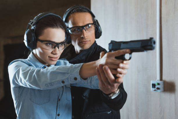 instructeur mâle aidant attrayant clients femmes détenant des armes à feu - gun men holding handgun photos et images de collection