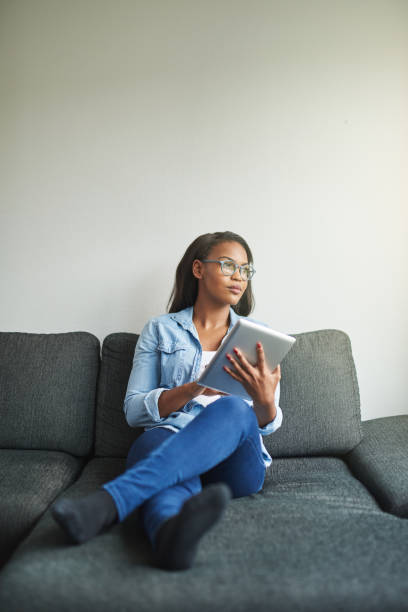 istock Young African woman relaxing on her couch busing a tablet 925439712