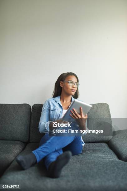 Young African Woman Relaxing On Her Couch Busing A Tablet Stock Photo - Download Image Now