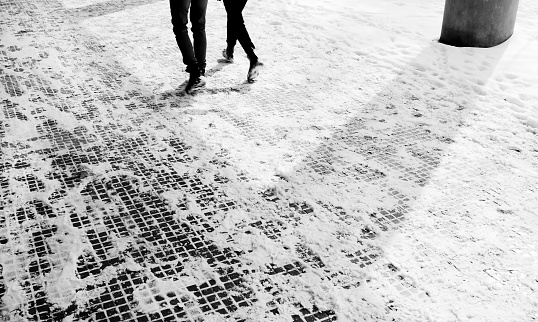 Legs of two people walking down the snowy sidewalk in motion blurin black and white