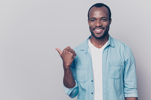 Portrait of handsome satisfied attractive cheerful joyful delightful afro guy dressed in casual clothing is showing aside on copyspace, isolated on grey background