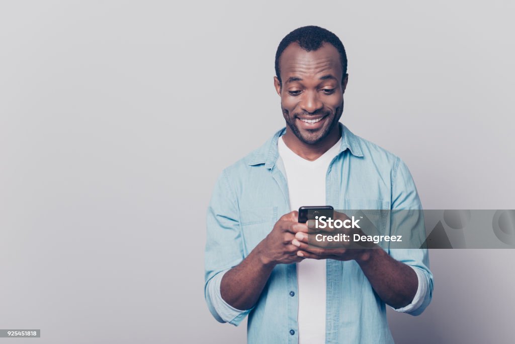 Portrait de beau heureux joyeux joyeux délicieux curieux mec porter décontractés jeans denim chemise envoyer et recevoir des messages à son amant isolé sur fond gris - Photo de Hommes libre de droits