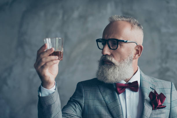 foto ravvicinata di serio pensieroso fiducioso soddisfatto ricco ricco imprenditore produttore di vino che guarda il bicchiere con whisky, isolato su sfondo grigio - pocket suit glasses jacket foto e immagini stock