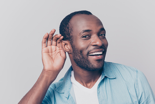 Close up portrait of curious interested delightful funny amazed cheerful surprised african man holding hand near ear and trying to hear the information isolated on gray background