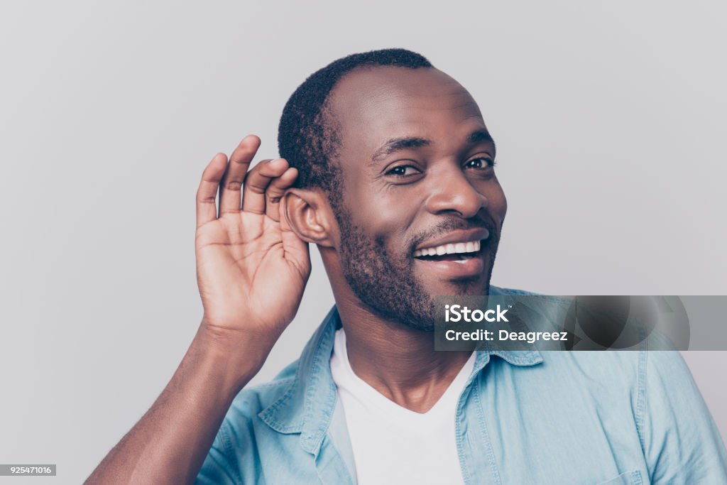 Close up portrait of curious interested delightful funny amazed cheerful surprised african man holding hand near ear and trying to hear the information isolated on gray background Ear Stock Photo