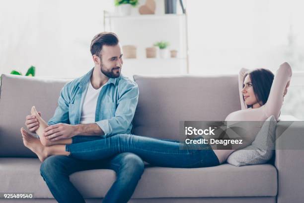 I Bliss Out And On Cloud Nine Attentive Caring Loving Handsome Bearded Husband Is Doing Feet Massage For Her Attractive Tender Lying On A Sofa Wife Stock Photo - Download Image Now