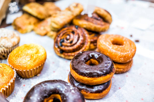Many different selection of pastry dessert sweets for continental breakfast, chocolate fried donuts, muffins, cinnamon rolls buns on paper tray in cafe, store, brunch, buffet, home
