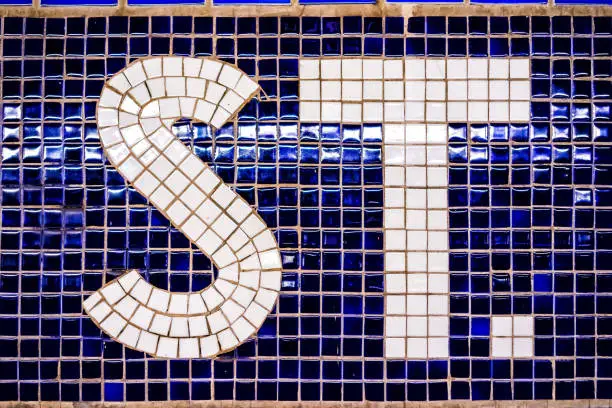 Closeup of abbreviated street st sign, period in purple blue colorful tile pattern background in New York City NYC Subway Station
