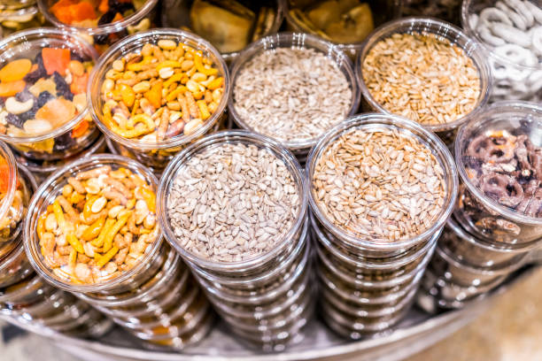 Many packaged seeds, nuts, dried fruit in plastic containers on display on store shop shelves, sunflower seeds mix, pretzels