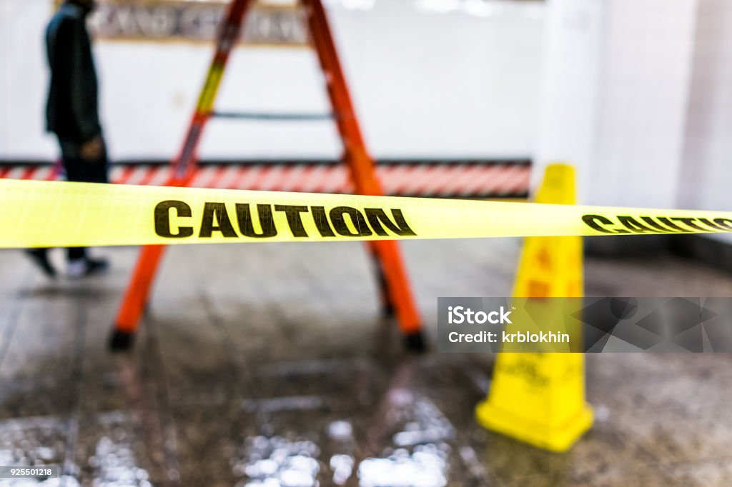 Caution tape sign in underground transit empty large platform in New York City NYC Subway Station in Grand Central, ladder, wet floor cone Adhesive Tape Stock Photo