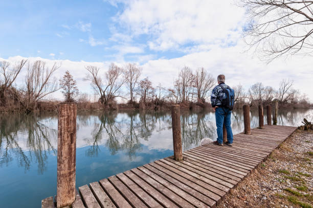 istock Hiker with backpack over wood pier on shore of river. 925501330