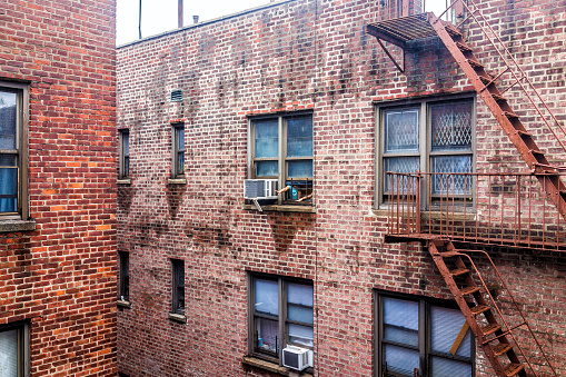 Bronx: Brick apartment condo building architecture in Fordham Heights, Bronx, NYC, Manhattan, New York City, fire escapes, windows, ac units during rain, kids children playing, reaching arms through window