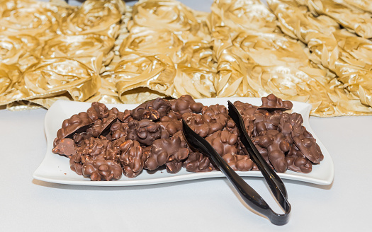 Arrangement or presentation of homemade chocolate covered peanut clusters at a birthday party event with white and gold as theme colors.