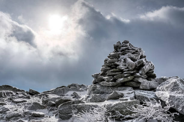 Cairn, pile of rocks at the summit during a winter cold day. Sun pierces through the clouds. Cairn, pile of rocks at the summit during a winter cold day. Sun pierces through the clouds. white mountains new hampshire stock pictures, royalty-free photos & images