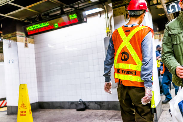 New York City: Employee worker inspecting leak in underground transit empty large platform in NYC Subway Station, wet floor sign slippery yellow cone