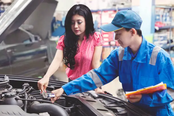 Car mechanic helping a customer fixing the car while holding a checklist