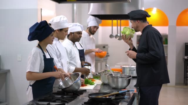 Head chef teaching his students about a healthy lettuce smelling it and letting other students smell all very focused and some smiling
