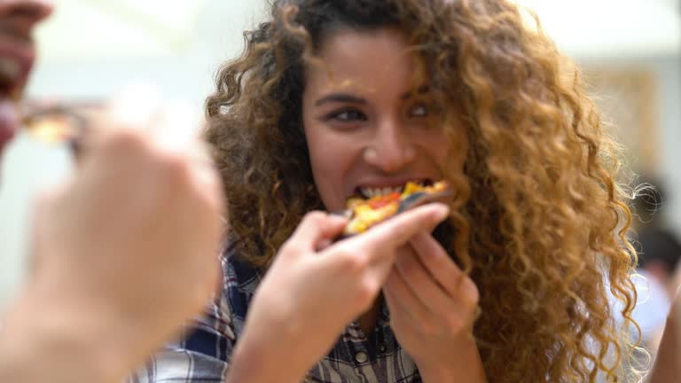 Close up of a beautiful woman with curly hair enjoying a pizza with her friends at a restaurant looking very happy
