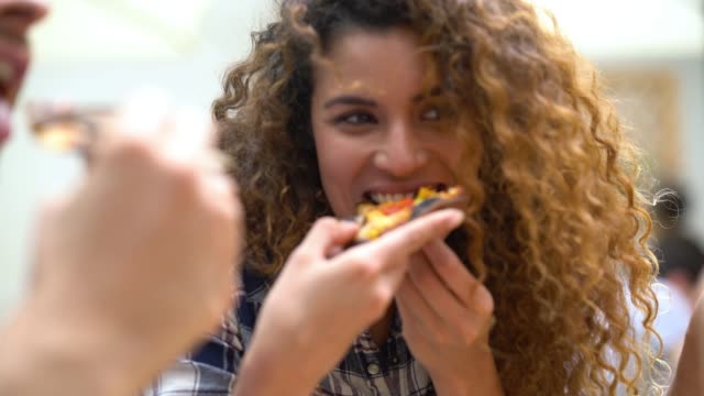 Close up of a beautiful woman with curly hair enjoying a pizza with her friends