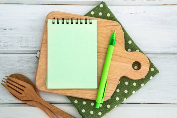 istock Notepad on chopping board with a wooden fork and spoon on white table , recipes food or diet plan for healthy habits shot note background concept 925574688