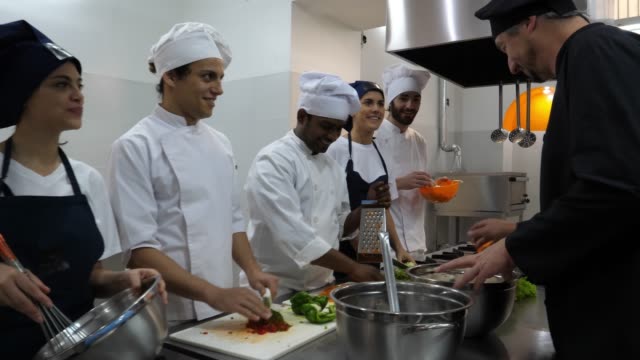 Male Chef teaching his students about the different ingredients and encouraging them to smell them all looking happy and smiling