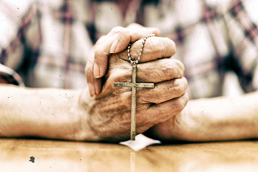 Color image depicting a senior caucasian man in his 60s in quiet prayer inside an old anglican church. The man has his hands clasped together in prayer. The man is alone and has his head bowed in solemn thought. Room for copy space.