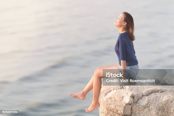 Mujer Con Casual Sentado En La Roca Acantilado Relajando Sonreír Y Respirar Profundo Aire Con Borrosa Mar Ola Foto de stock y más banco de imágenes de Ejercicios de respiración