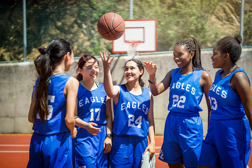 Multi-ethnic female athletes standing on court. Basketball players are throwing ball at high school. They are wearing blue sports uniform.