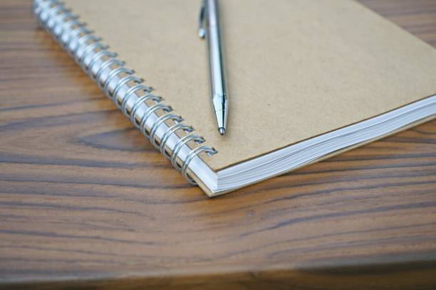 istock Brown notebook and silver pen with wooden table texture background 925618526