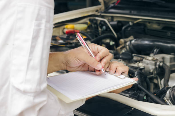istock Selective focus on hands of professional young Asian mechanic man in uniform writing on clipboard against car in open hood at the repair garage. Maintenance service concept. 925619144