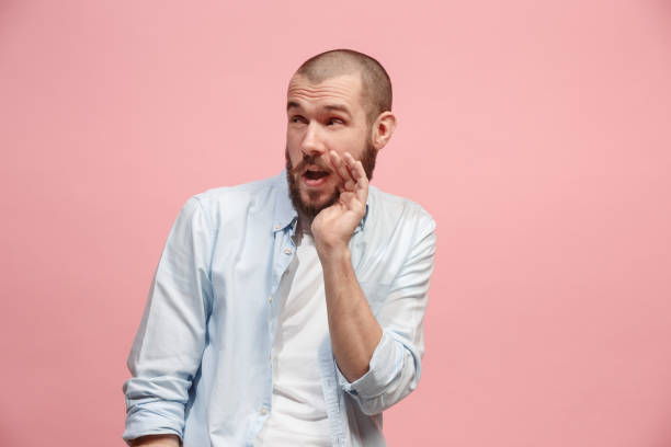 istock The young man whispering a secret behind her hand over pink background 925622840