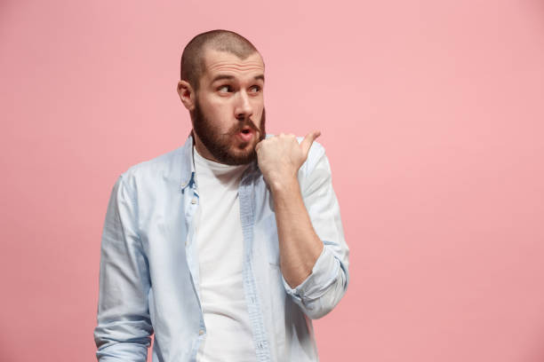 istock The young man whispering a secret behind her hand over pink background 925622878