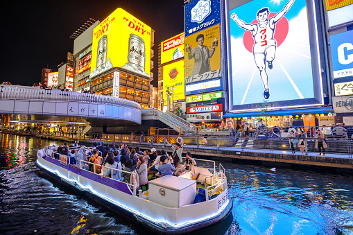 Osaka, Japan - April 29, 2017: touristic boat in Dotonbori Canal and famous Glico Running Man sign in Dotonbori street, Namba, a popular shopping and entertainment district. Nightlife and night scene.